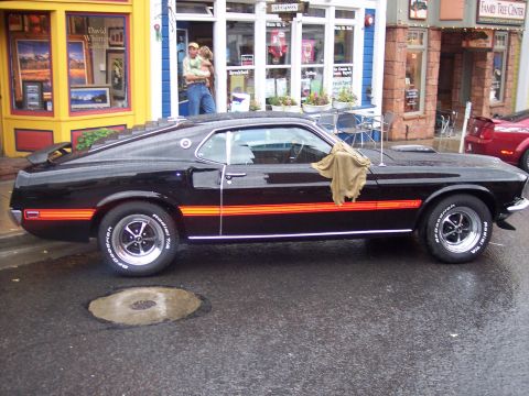 Black Ford Mustang Mach 1 fastback with orange stripes parked on wet street