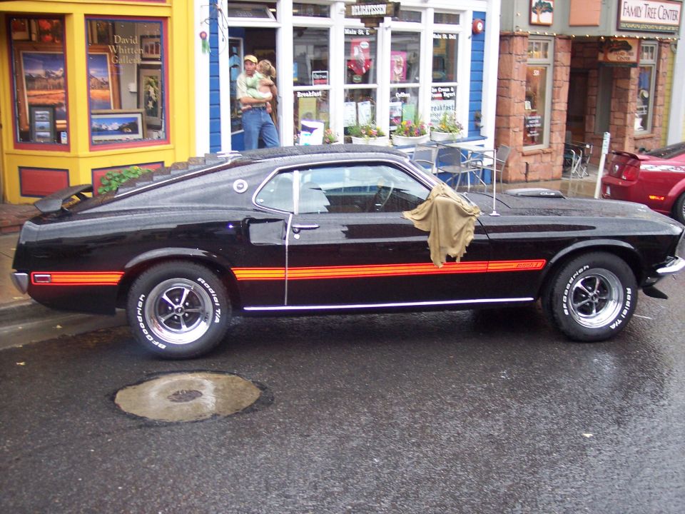 Black Ford Mustang Mach 1 fastback with orange stripes parked on wet street