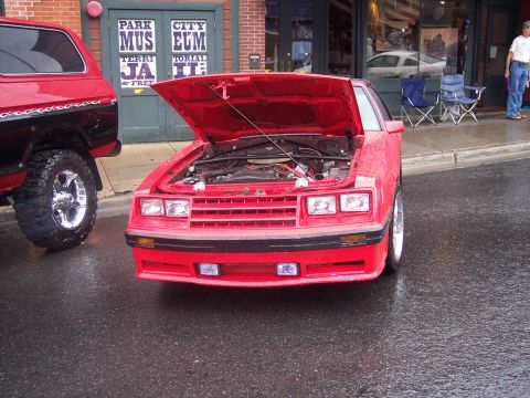 Red Fox-body Ford Mustang coupe with hood up on wet street at car show