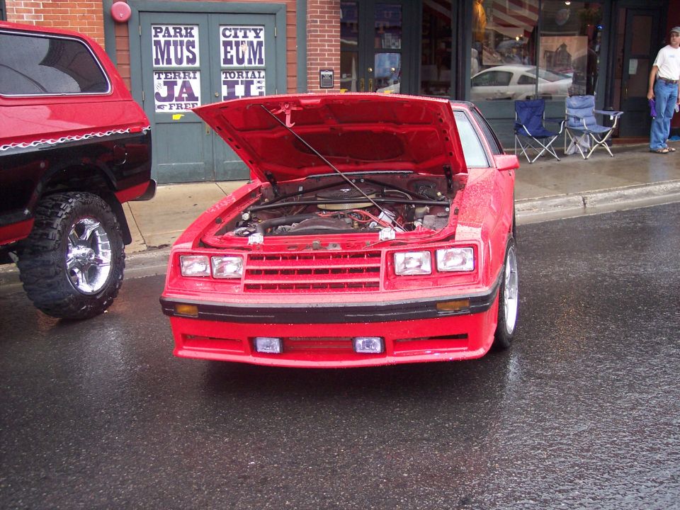 Red Fox-body Ford Mustang coupe with hood up on wet street at car show