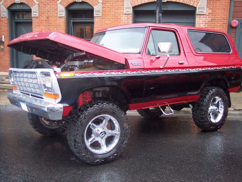 Red and black lifted Ford Bronco SUV with hood open on wet street