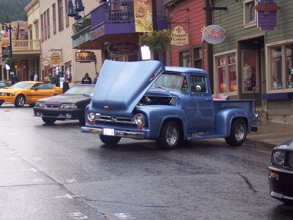 Light blue vintage Ford pickup with open hood on a wet downtown street