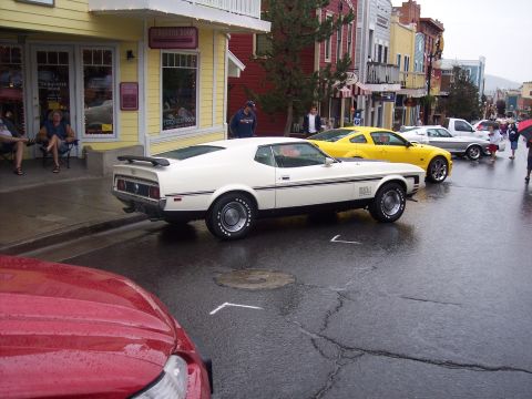 White Ford Mustang Mach 1 fastback rear 3/4 view on wet street at a car show
