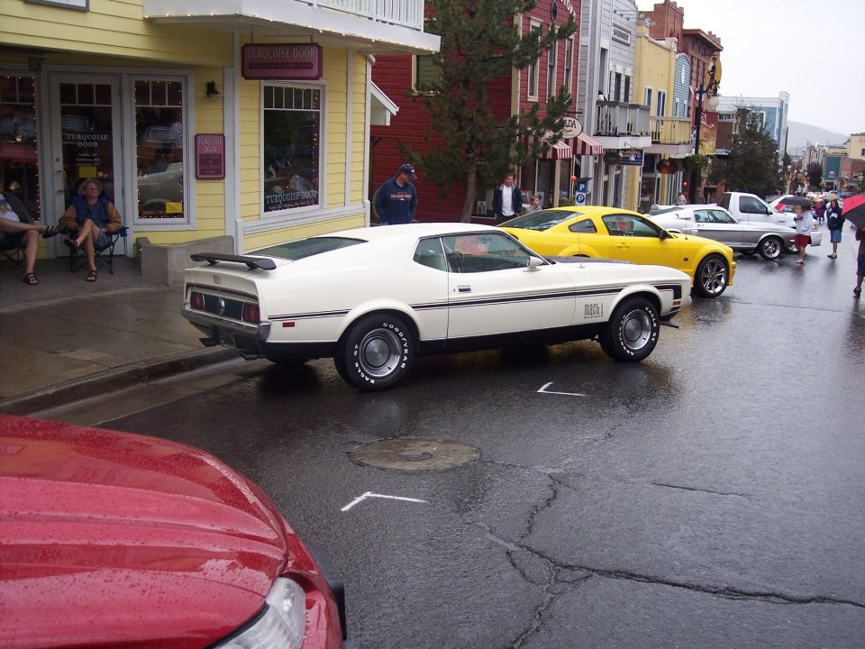 White Ford Mustang Mach 1 fastback rear 3/4 view on wet street at a car show