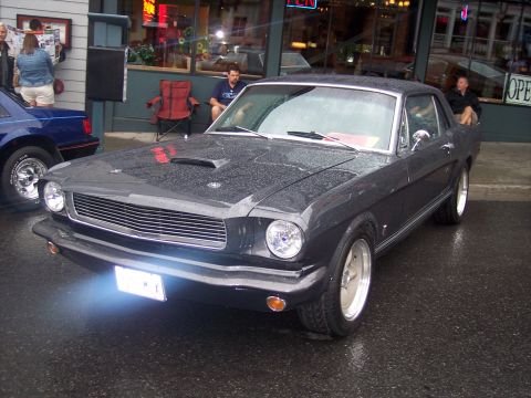Dark gray classic Ford Mustang coupe, 3/4 front view, on wet street at a car show