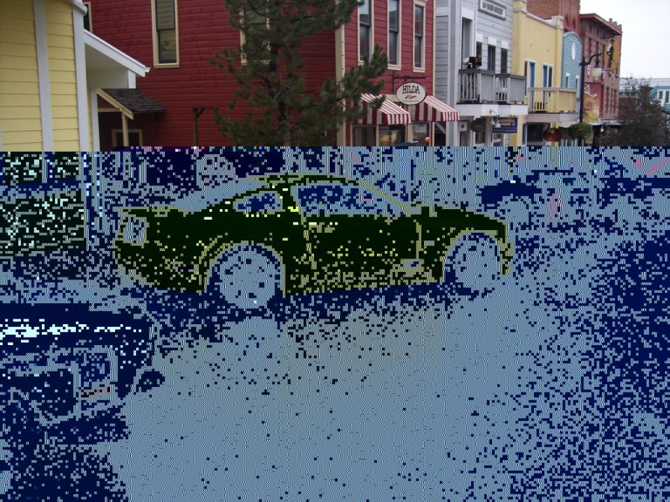 Corrupted side view of a car parked in front of colorful downtown storefronts