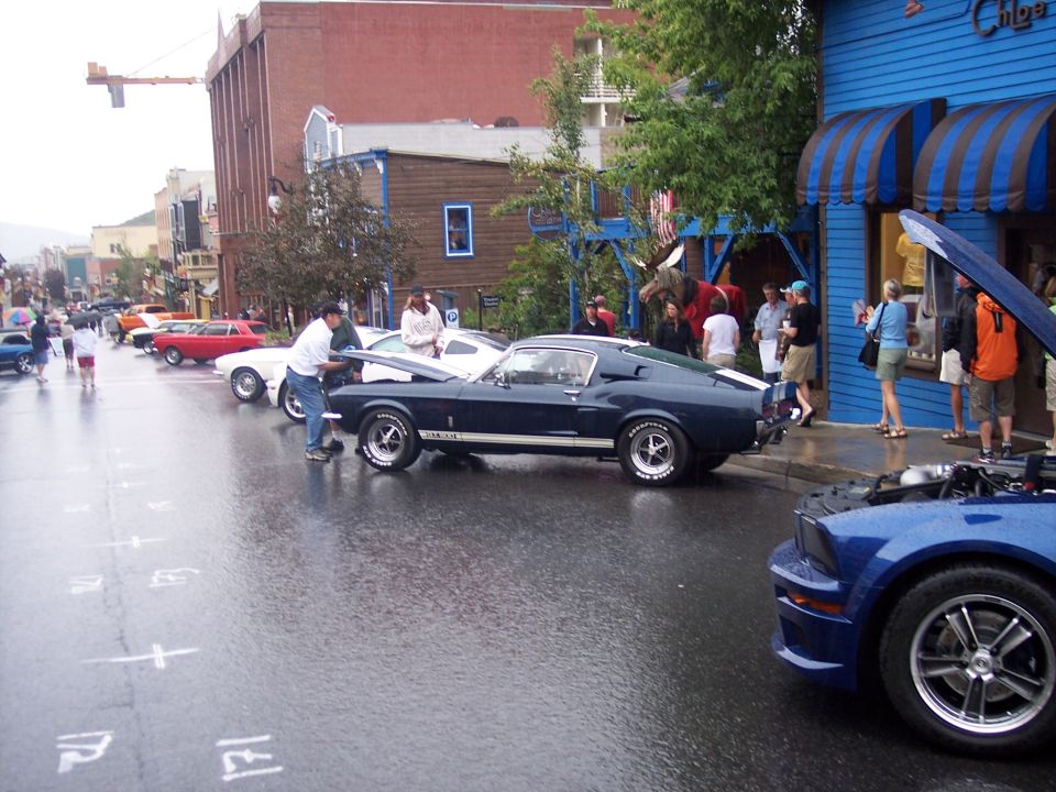 Dark fastback coupe with white stripes at a rainy street car show