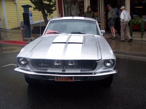 Silver classic Mustang fastback with blue racing stripes, front view on wet street