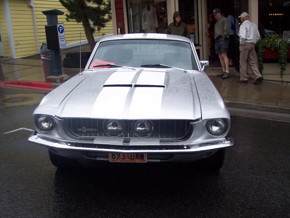 Silver classic Mustang fastback with blue racing stripes, front view on wet street