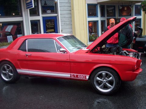 Red coupe, side view, hood up, white 'G.T. 680' stripes, parked by shops