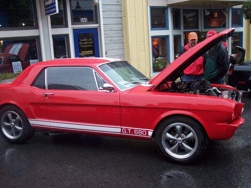 Red coupe, side view, hood up, white 'G.T. 680' stripes, parked by shops