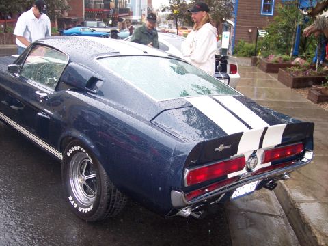 Dark blue Mustang fastback with white stripes, rear 3/4 view on wet street