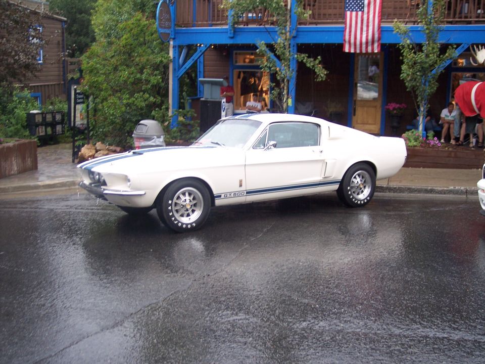 White Mustang fastback with blue stripes and GT500 badge on wet street