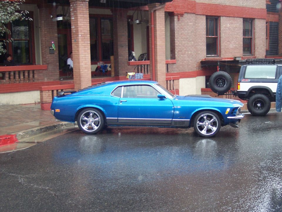 Blue classic Mustang fastback in side profile on wet street by brick building