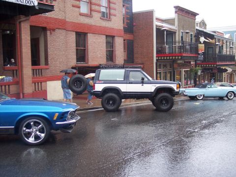 Lifted white SUV, blue muscle car and classic convertible on a wet downtown street