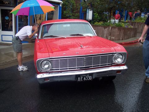 Front view of red Ford with chrome grille and Utah plate on wet street, man with rainbow umbrella looking insi