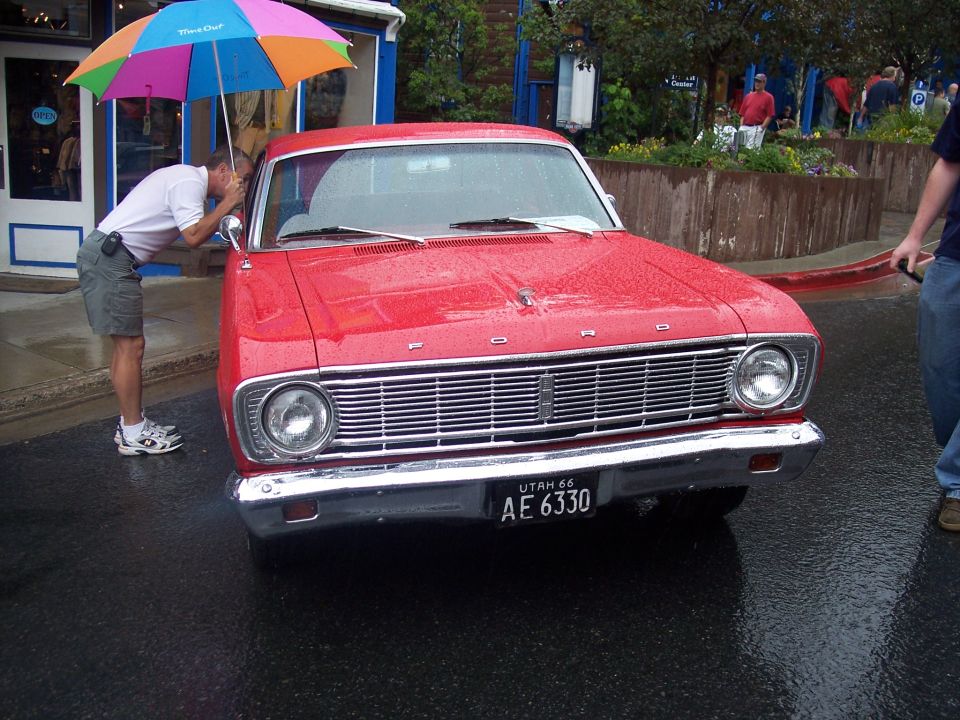 Front view of red Ford with chrome grille and Utah plate on wet street, man with rainbow umbrella looking inside