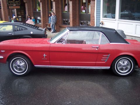 Red Ford Mustang convertible with black top parked in profile on a wet street