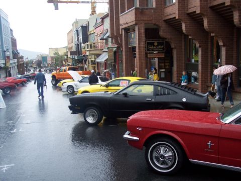 Red convertible and black fastback at a rainy street classic car show