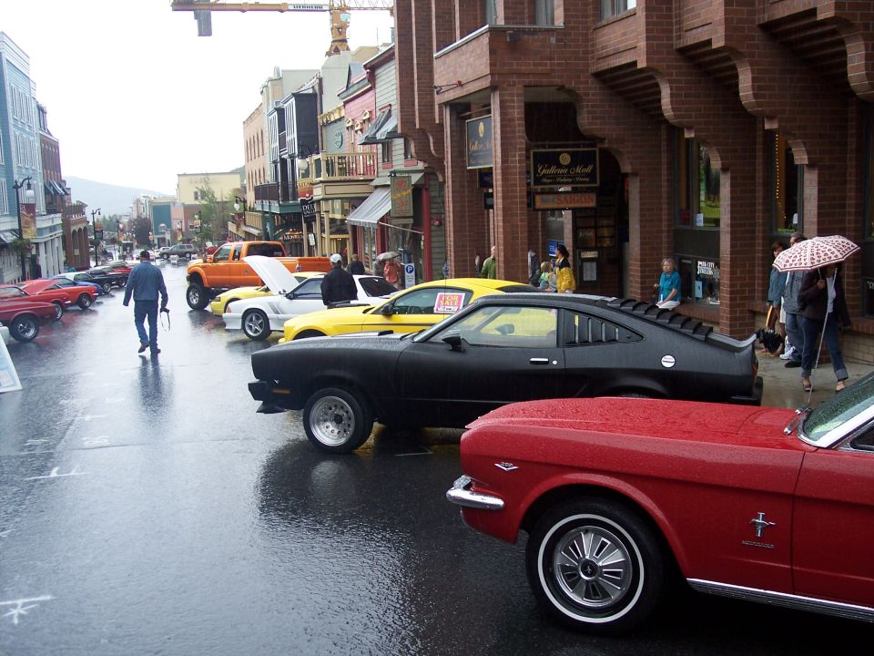 Red convertible and black fastback at a rainy street classic car show