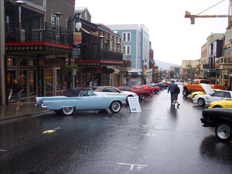 Light blue vintage Thunderbird convertible at a rainy street car show with other classics lined up.