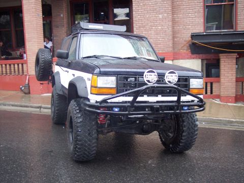Lifted black and white SUV with tube bumper and Hella lights on wet street