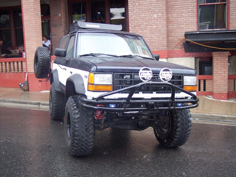 Lifted black and white SUV with tube bumper and Hella lights on wet street