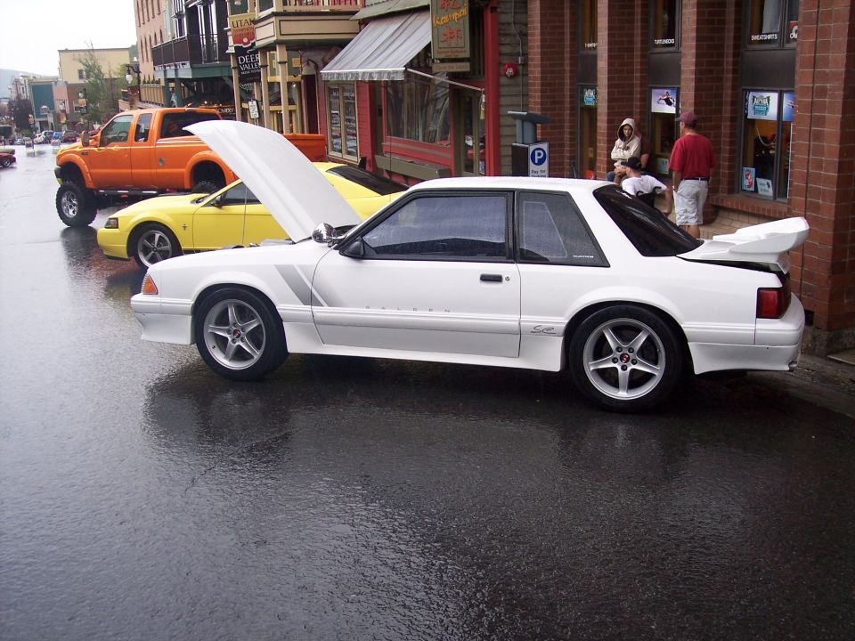 White Fox-body Mustang coupe with open hood and rear wing on wet street