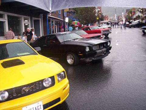 Yellow, black-striped, and red Mustangs at a rainy street car show
