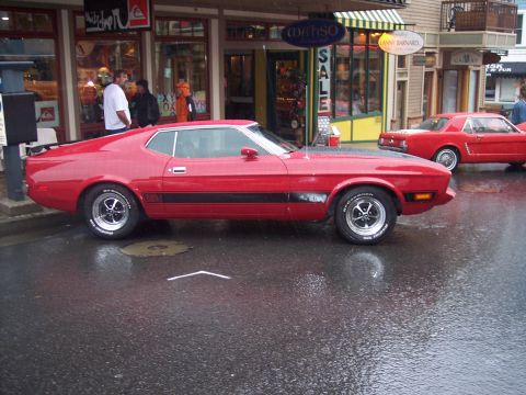 Red 1971-73 Ford Mustang fastback with black stripes and spoiler parked on a wet street