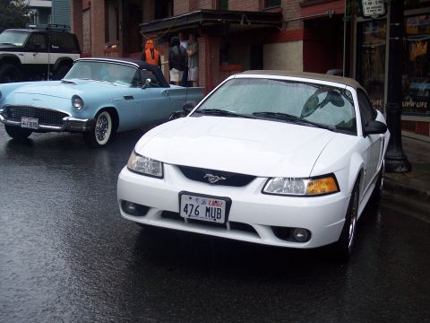 White Mustang convertible on wet street with blue vintage Thunderbird behind