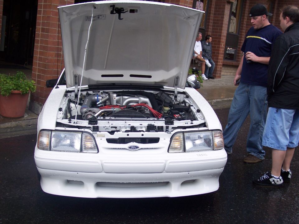 White Fox-body Mustang with open hood showing turbo engine, men standing beside it