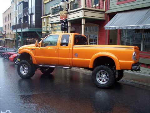 Orange lifted Ford Super Duty pickup on chrome wheels parked on a wet street.