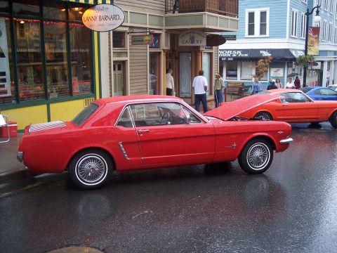 Red classic Mustang coupe, side view, on wet street with shops behind
