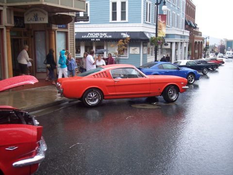 Orange classic Mustang fastback on a wet street with other cars and shops