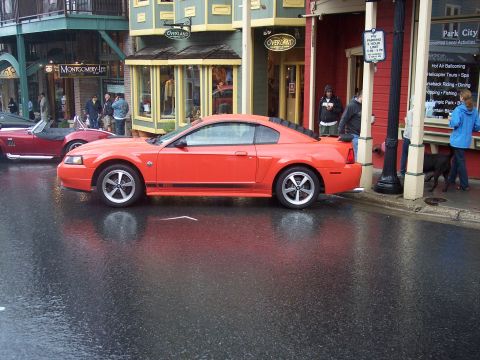 Orange Ford Mustang coupe, side view, parked on wet city street