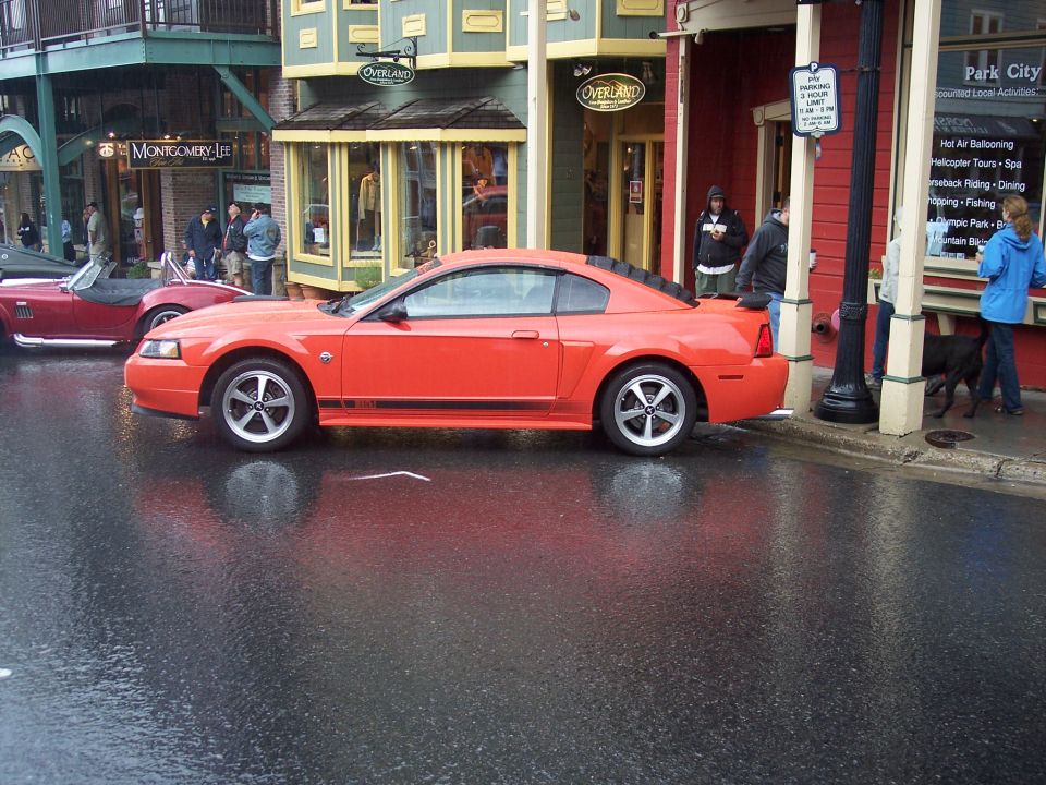 Orange Ford Mustang coupe, side view, parked on wet city street