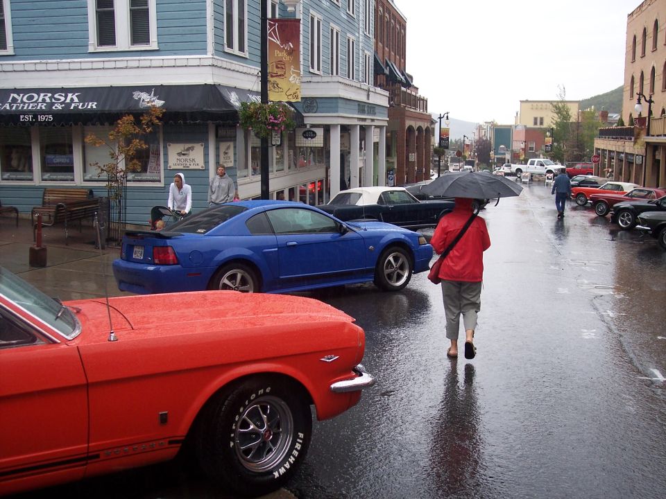 Red classic Mustang and blue Mustang on a wet downtown street, pedestrian with umbrella