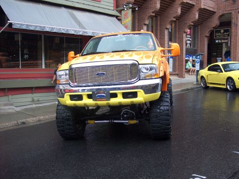 Yellow lifted Ford pickup with flame graphics, front view on wet street