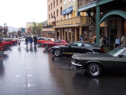 Classic Mustangs parked along a wet downtown street during a car show