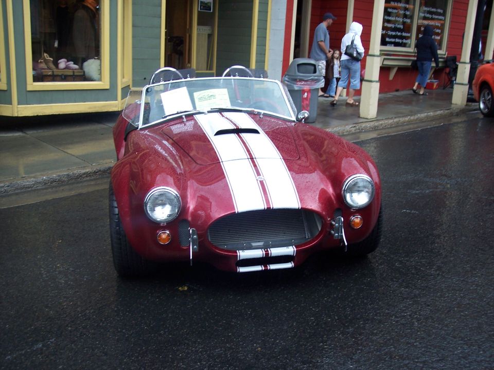Red Cobra-style roadster with white stripes, front view on wet street