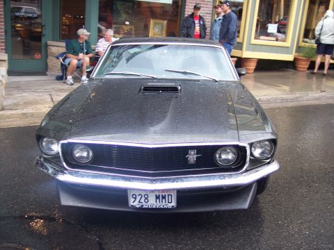 Front view of a black classic Ford Mustang with '928 MMD' plate on a wet street