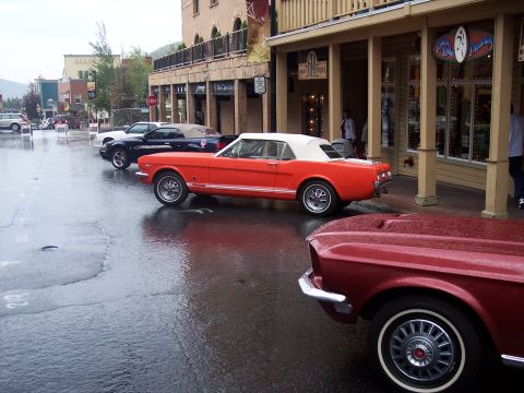 Orange white-top convertible on wet street with red car fender and wire wheel in foreground