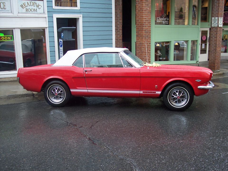 Red Ford Mustang convertible with white top parked in profile on a wet street