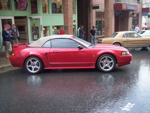 Red Mustang convertible with tan top, side view on wet city street