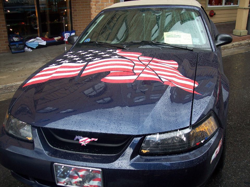 Dark blue Mustang convertible with American flag hood graphic, wet from rain