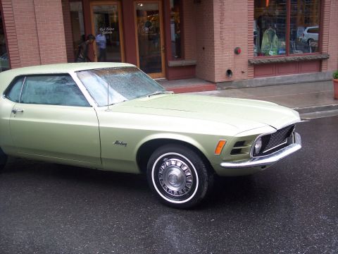 Light green vintage Ford Mustang coupe parked on a wet street, front 3/4 view