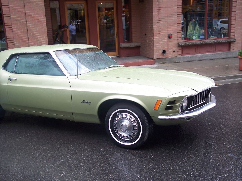 Light green vintage Ford Mustang coupe parked on a wet street, front 3/4 view