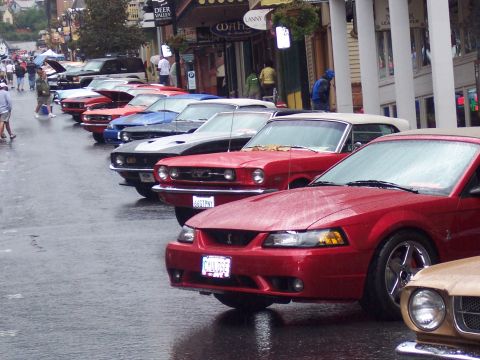 Row of classic red and blue Ford Mustangs parked along a wet street at a car show