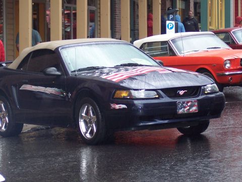 Dark blue Mustang convertible with American flag hood graphics on a wet street